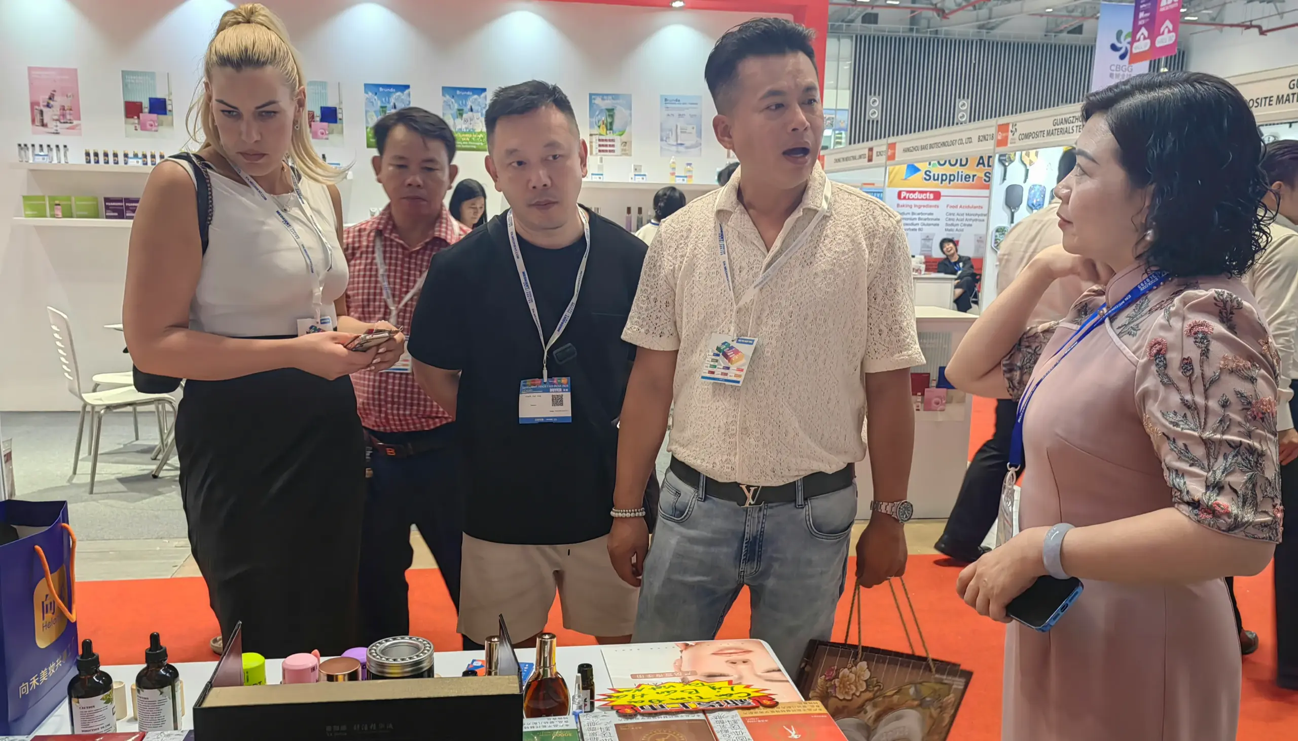 Visitors at a trade show booth examining beauty and health products displayed on a table.