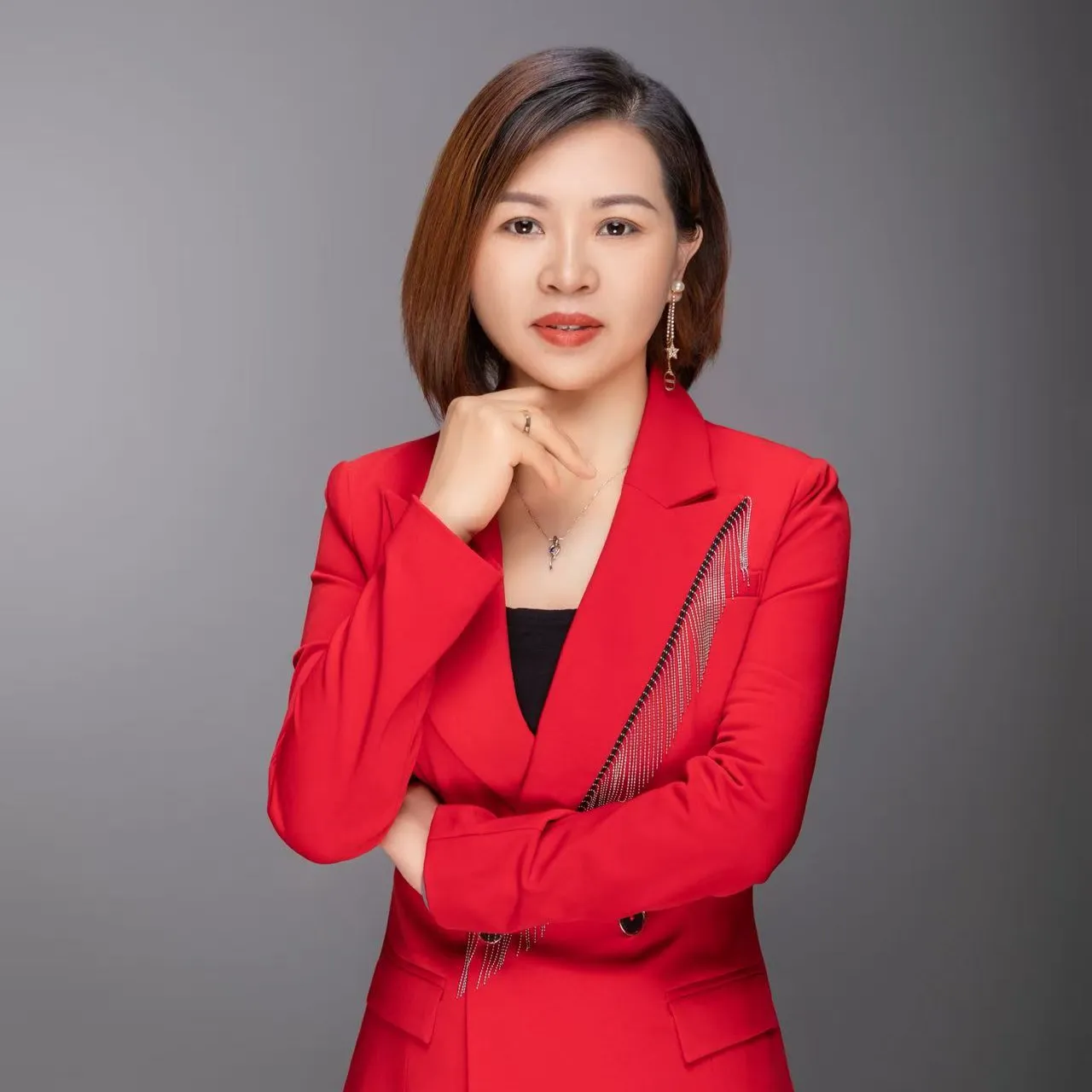 Professional portrait of Sister Tao wearing a red blazer with fringe details, posing against a grey background
